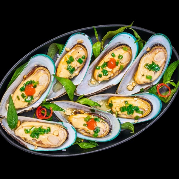A black platter of The Roasted Crab's mussels, garnished with herbs, chili, and sauce.