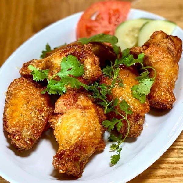Crispy fried chicken wings garnished with fresh cilantro, served with tomato and cucumber slices.