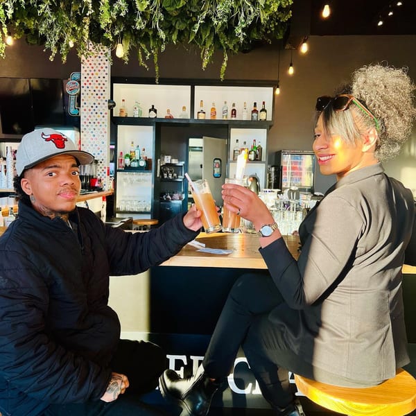 Two people clinking glasses with drinks at The Roasted Crab bar, featuring a lush green ceiling.