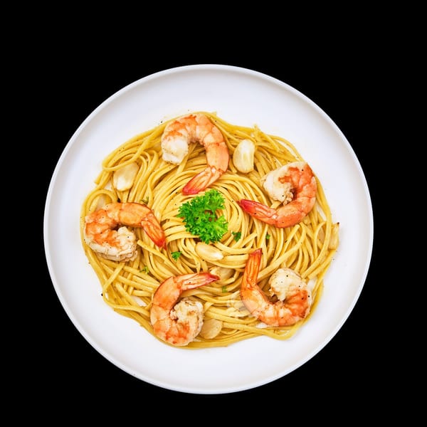 Shrimp scampi with linguine pasta, garlic, and parsley on a white plate.