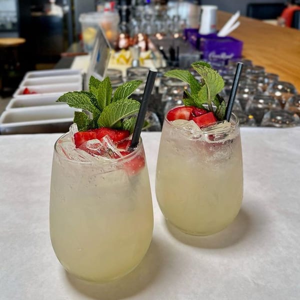 Two refreshing cocktails with strawberries, mint, and ice on a bar counter.