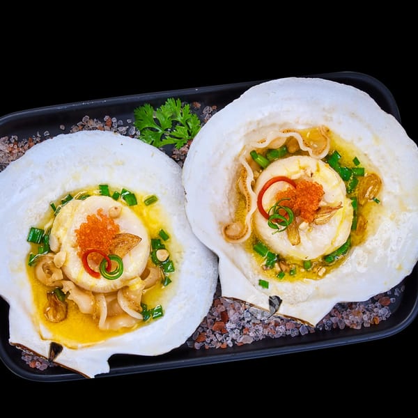 Two baked scallops in shells with butter, roe, garlic, and green onions on a bed of salt.